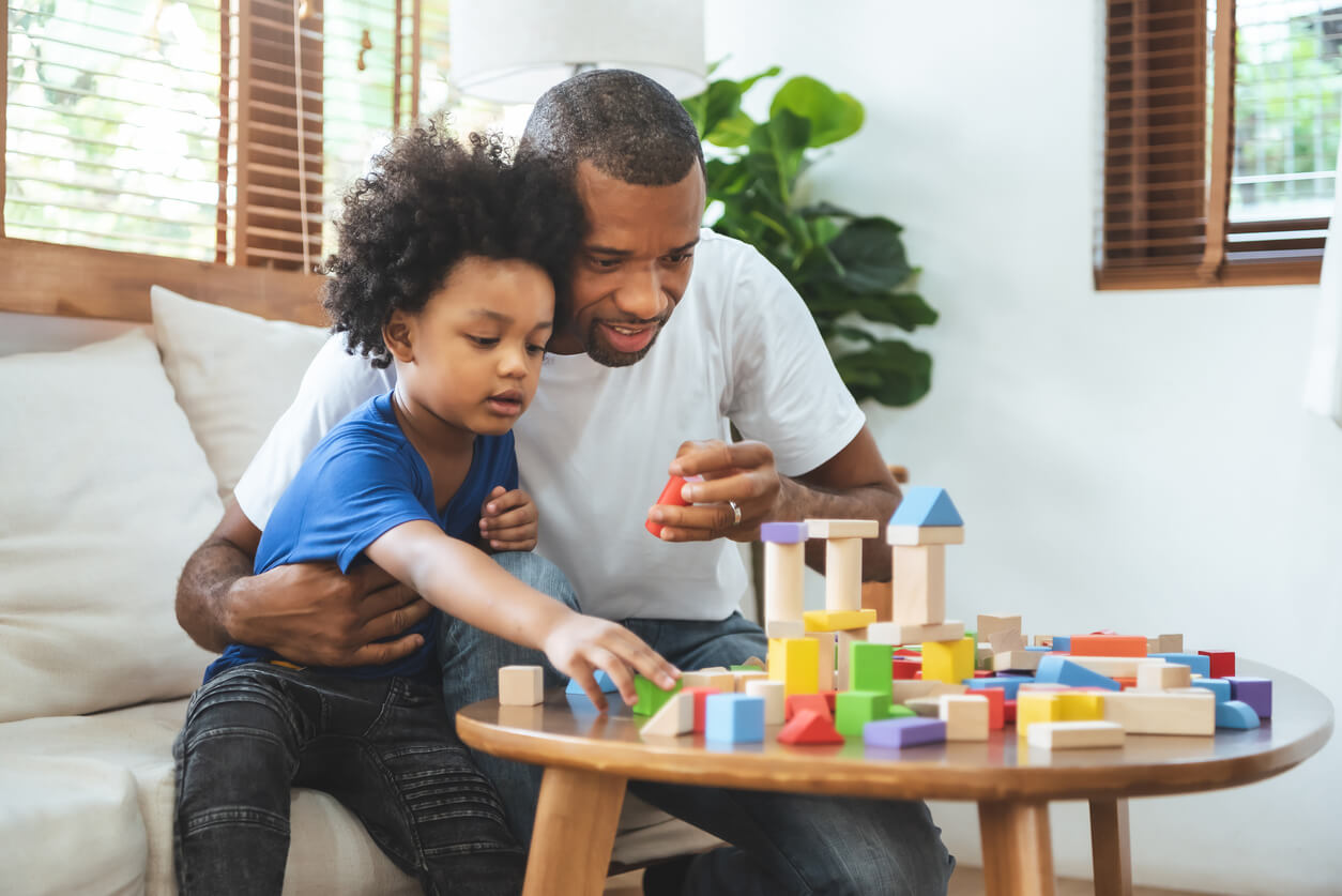 A black father and his son playing with building blocks.