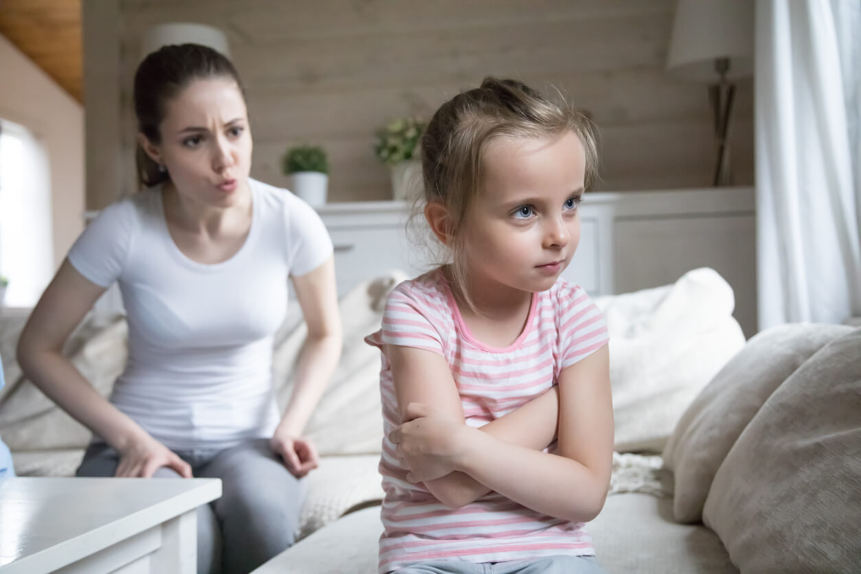 A little girl crossing her arms and turning her back to her mother, who is scolding her.