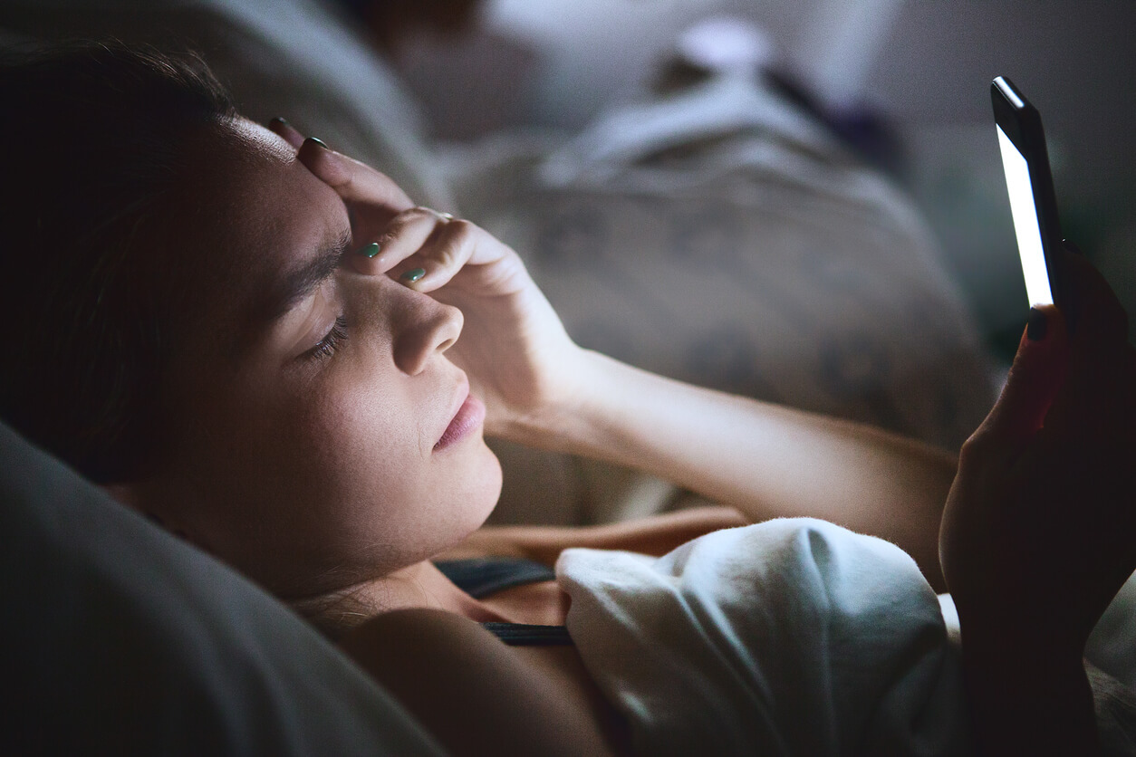 A teenager looking at her cell phone in the middle of the night.