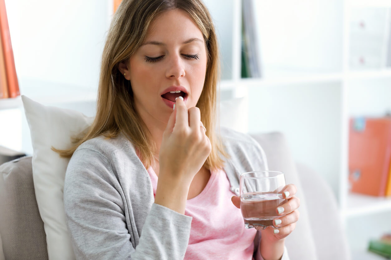 A woman taking a pill with a glass of water.