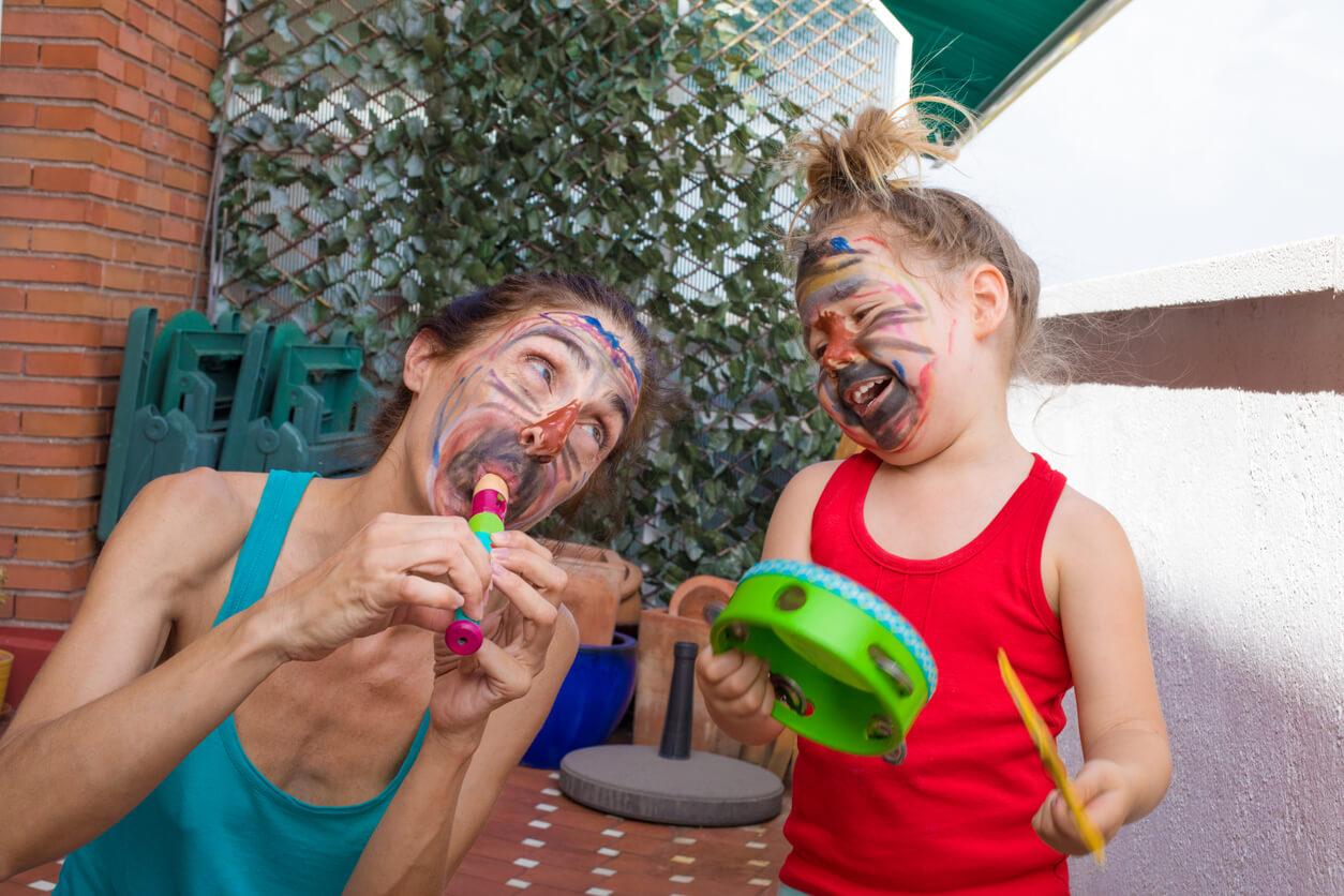A mother and her young daughter playing toy instruments with their faces painted with marker.