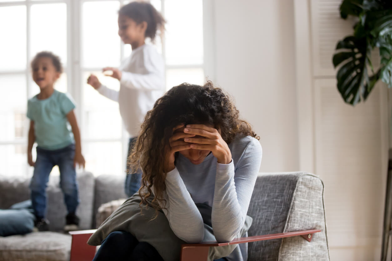 Children jumping on the couch while their mother feels overwhelmed.
