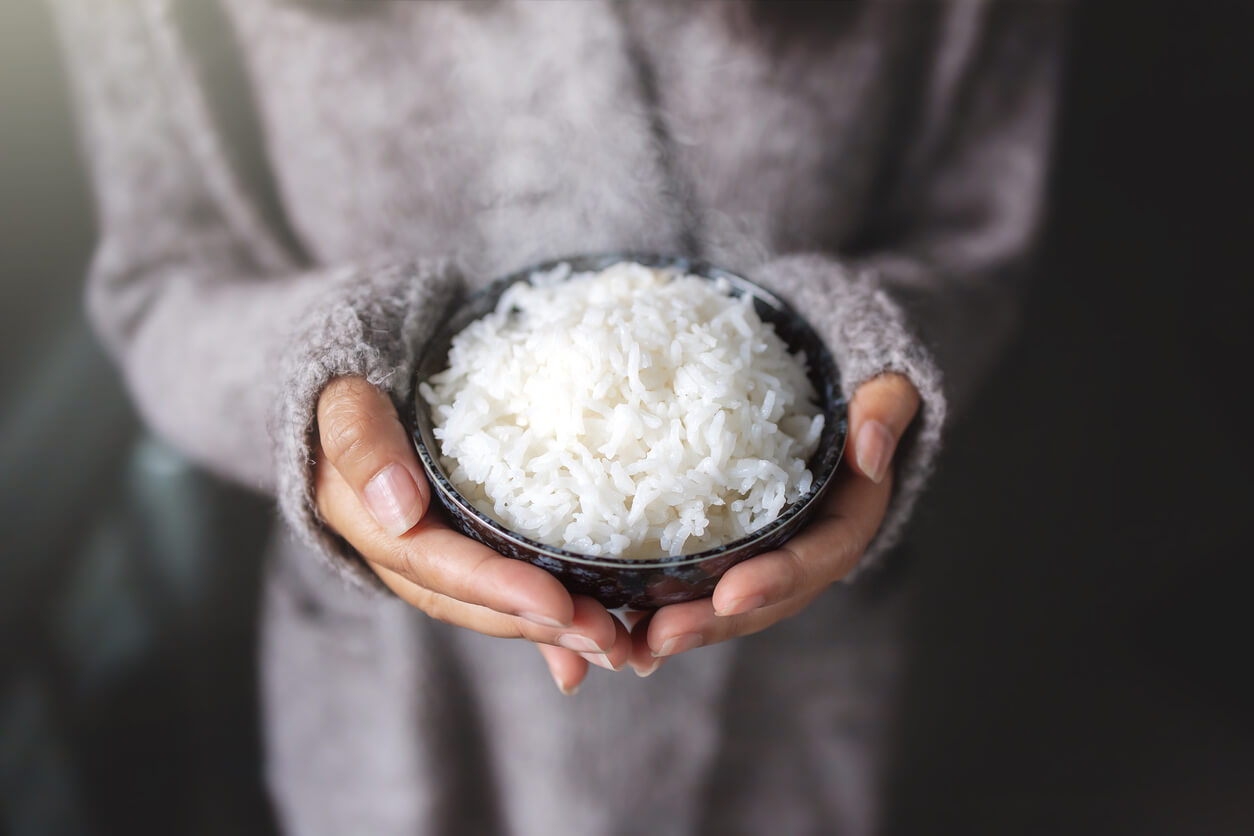 A woman holding a bowl of cooked white rice.