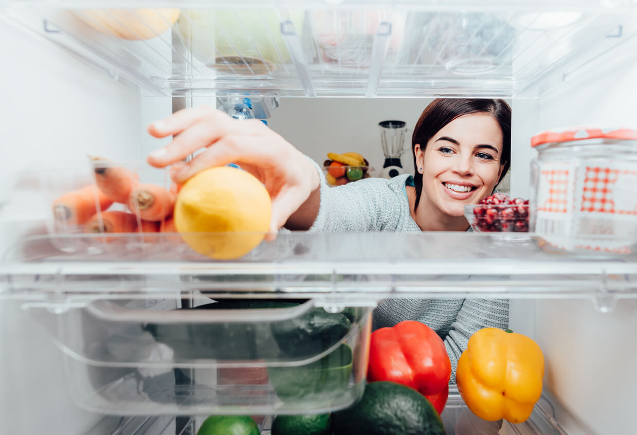 A woman grabbing a lemon from the refridgerator.