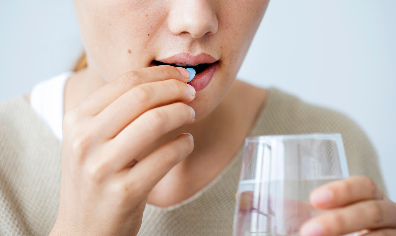 A woman swallowing a pill with water.