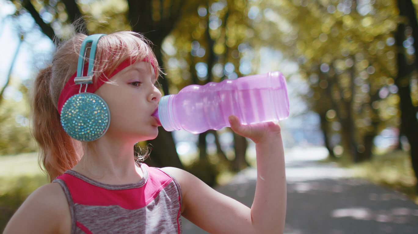 A young girl drinking from a water bottle while in the park.