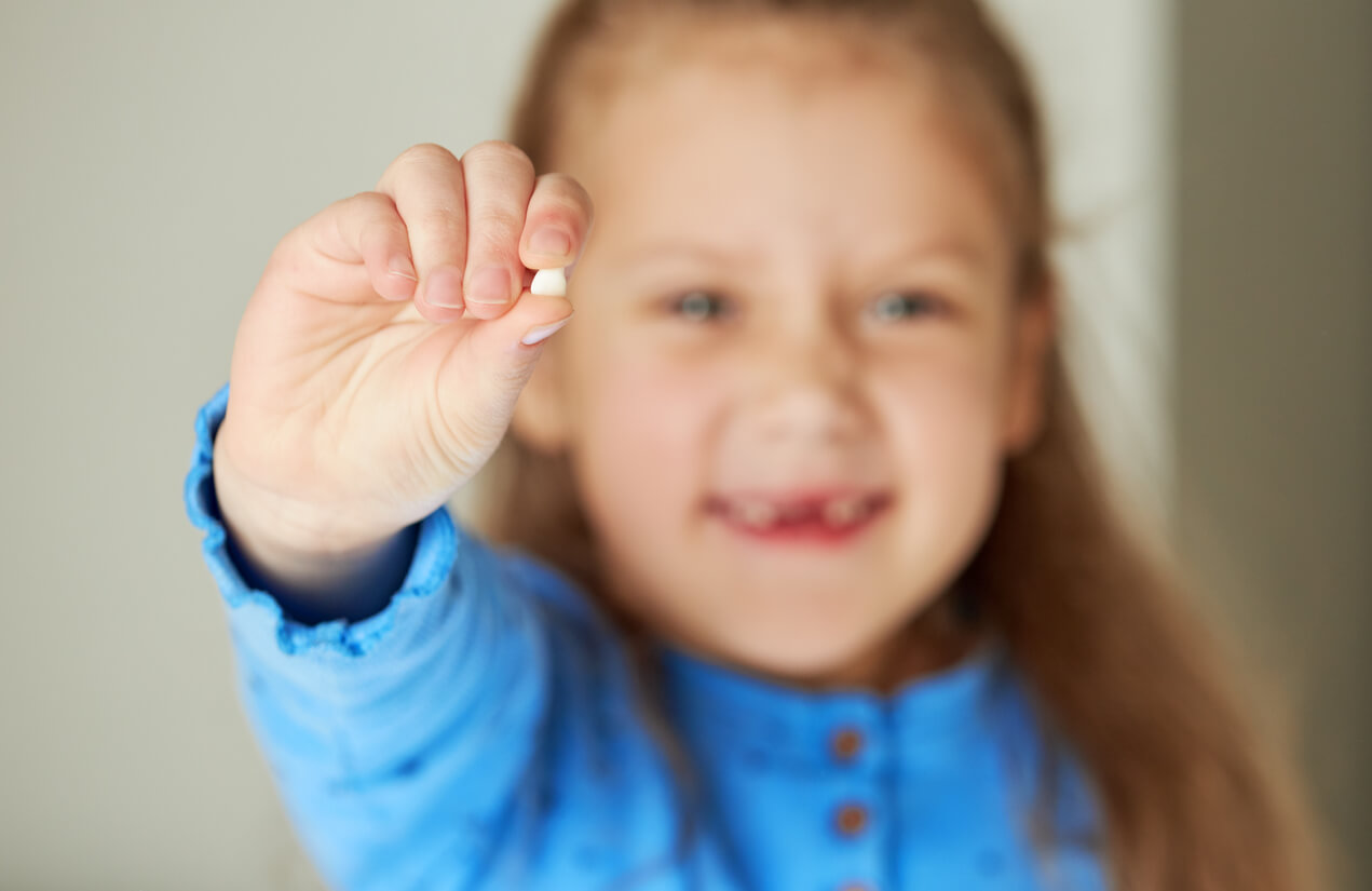 Une petite fille avec une dent de lait dans la main.