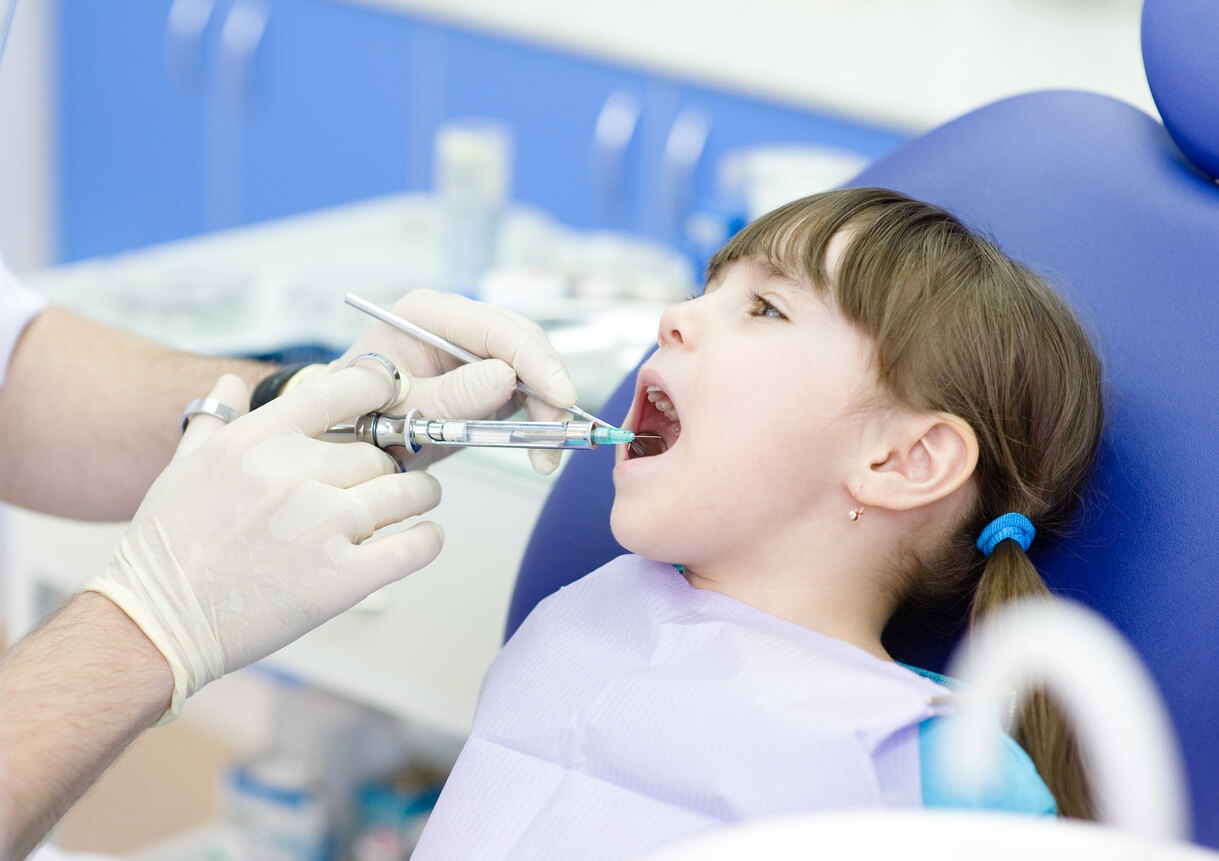 A dentist giving a little girl and injection before performing a dental procedure.