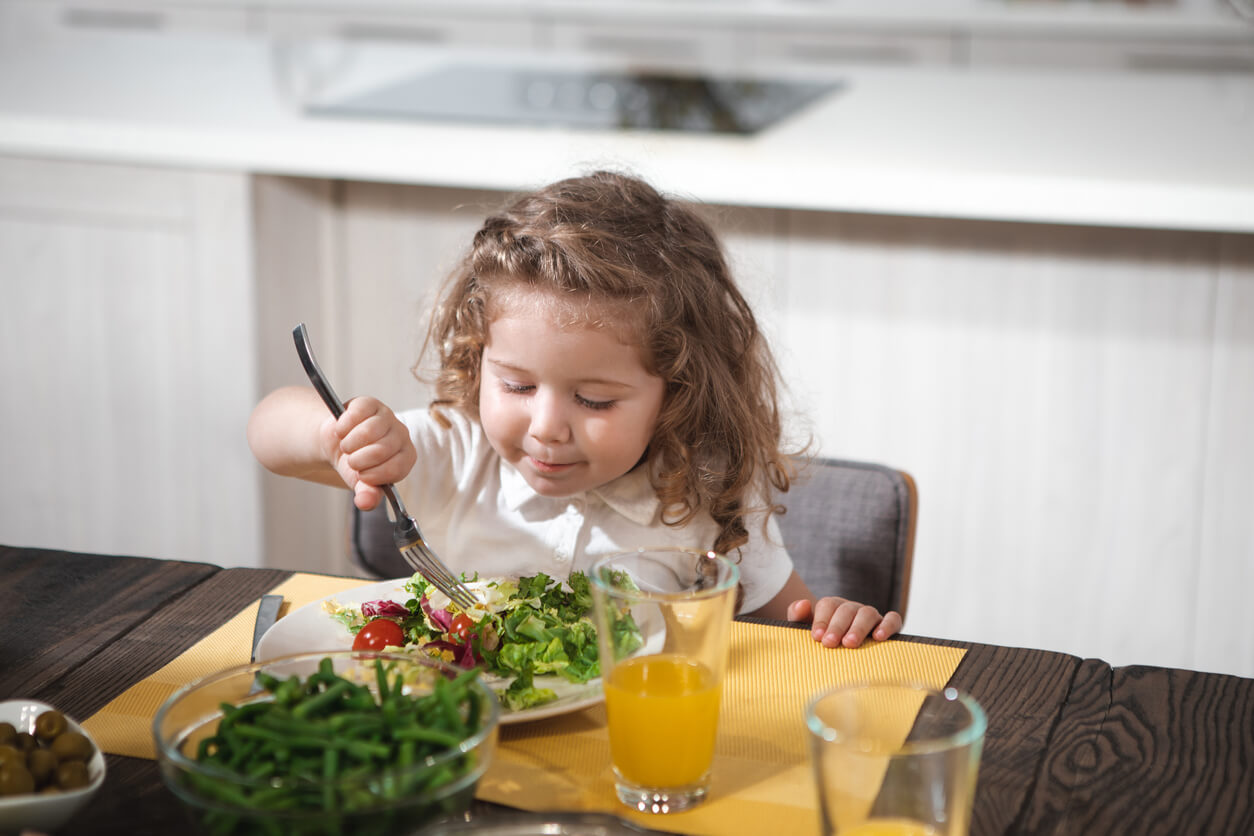A toddler girl eating a plate of vegetables.