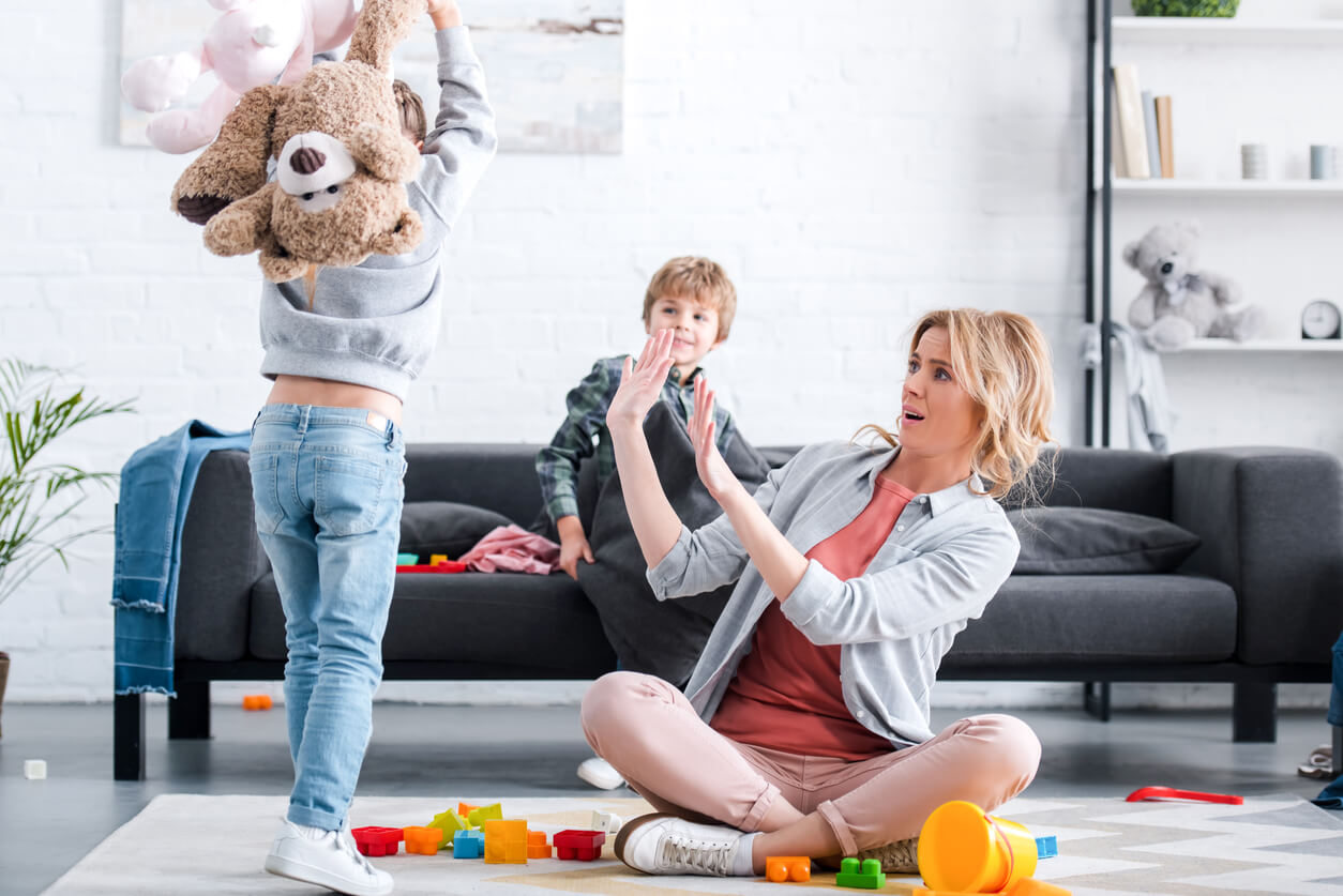 A mother holding up her hands as her child's is about the hit her with a stuffed animal.