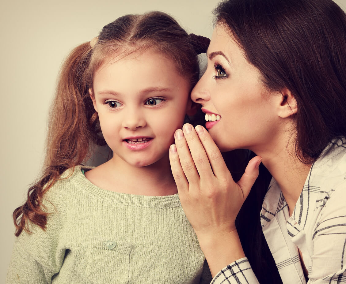 A woman whispering in a young girl's ear.
