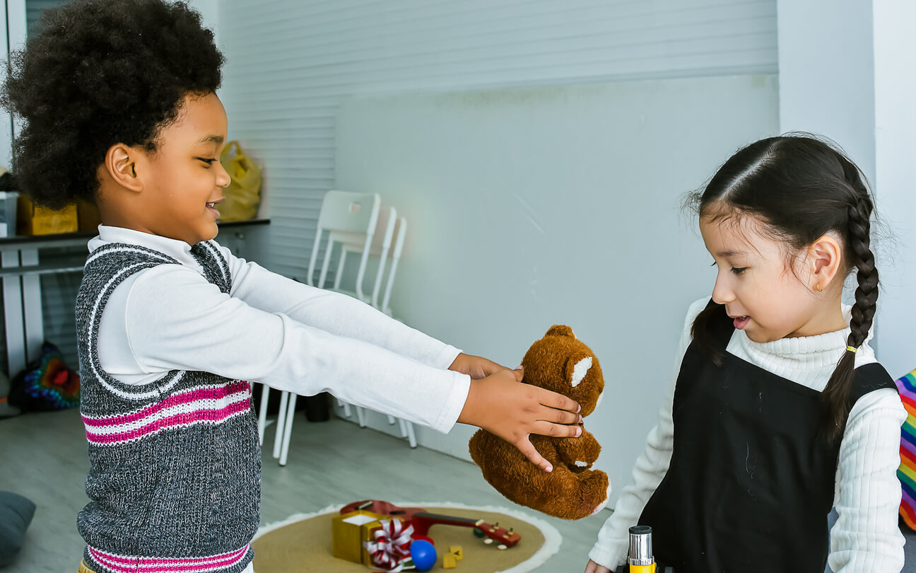 A child giving a teddy bear to another child.