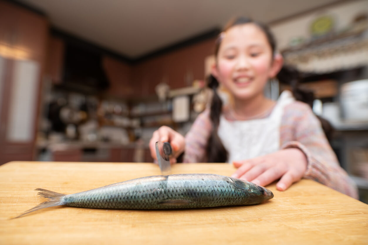 An Asian girl cutting a fish on a cutting board.