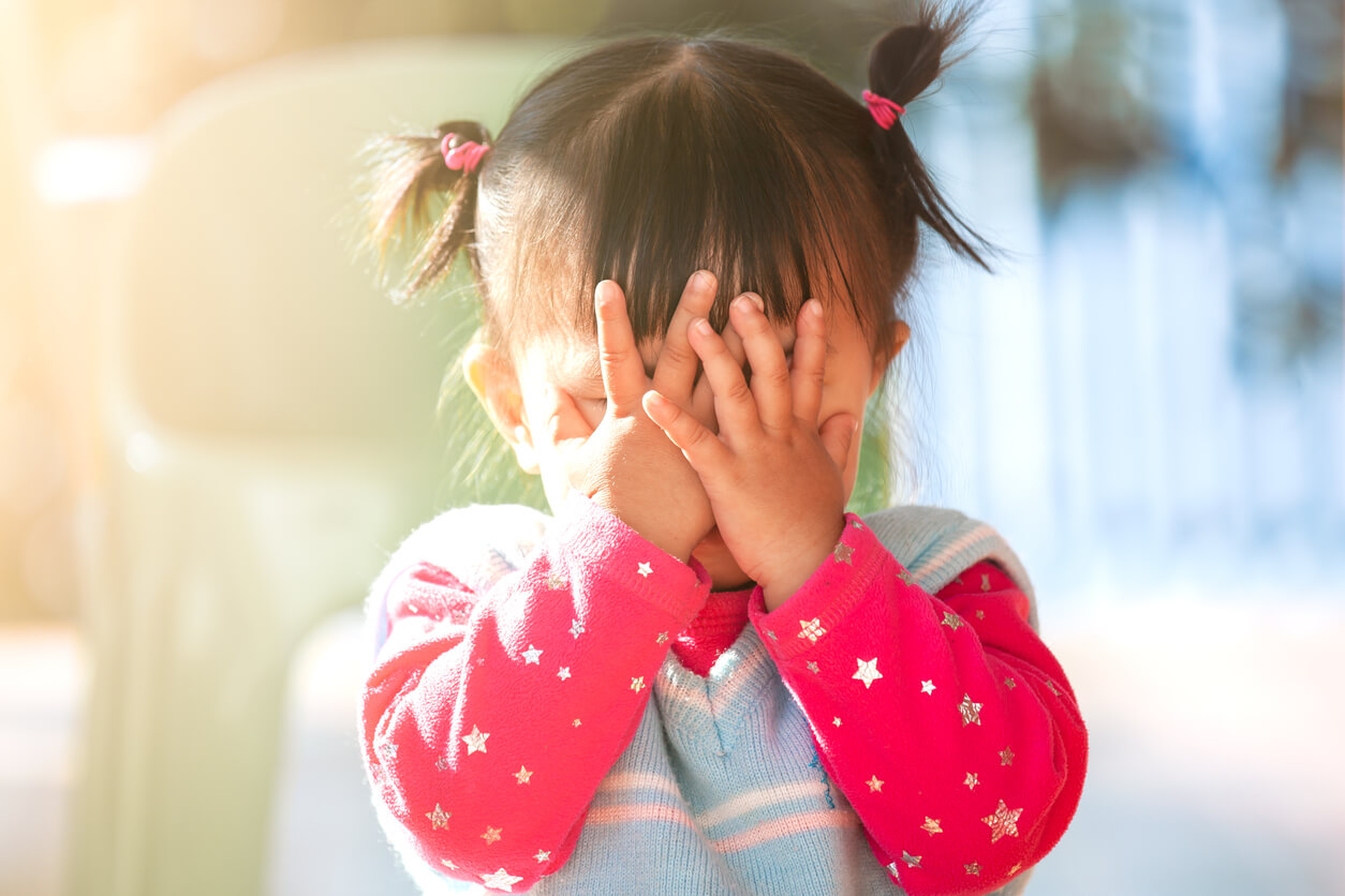 A toddler girl covering her face.