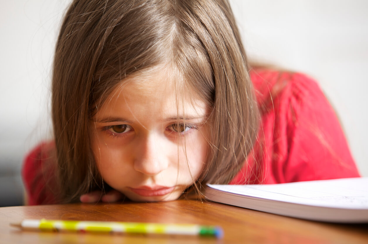A young girl resting her chin sadly on her desk.