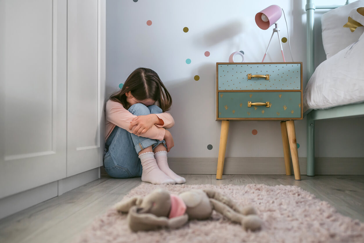A young girl sitting in the corner of her room, crying.