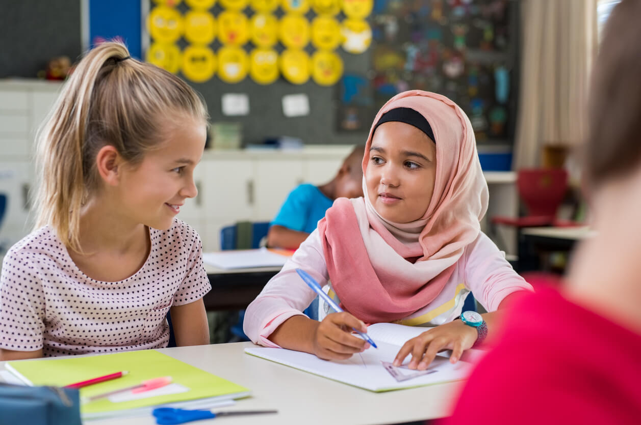Two children, one of whom is wearing a hijab, working together in class.