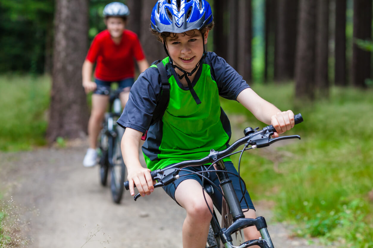 Children riding bikes on a path in the woods while wearing helmets.