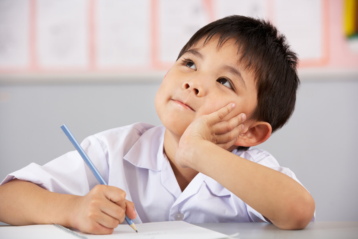 An Asian boy sitting in class, daydreaming.