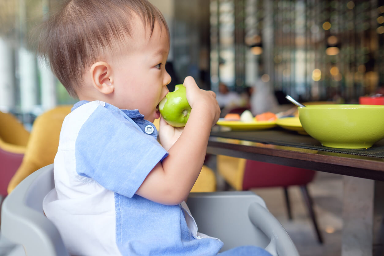 En asiatisk baby som spiser et grønt eple.