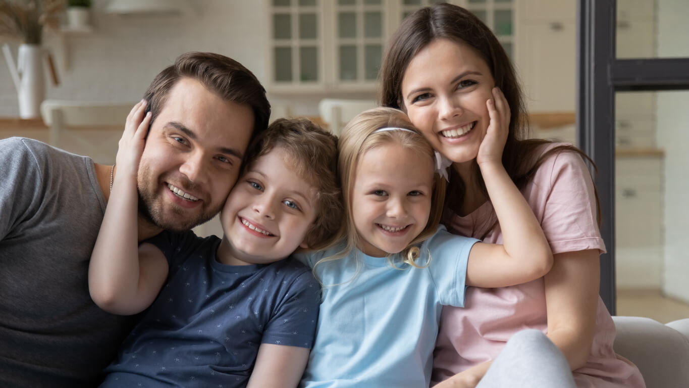 A small boy and girl sitting with their parents on the couch and smiling.