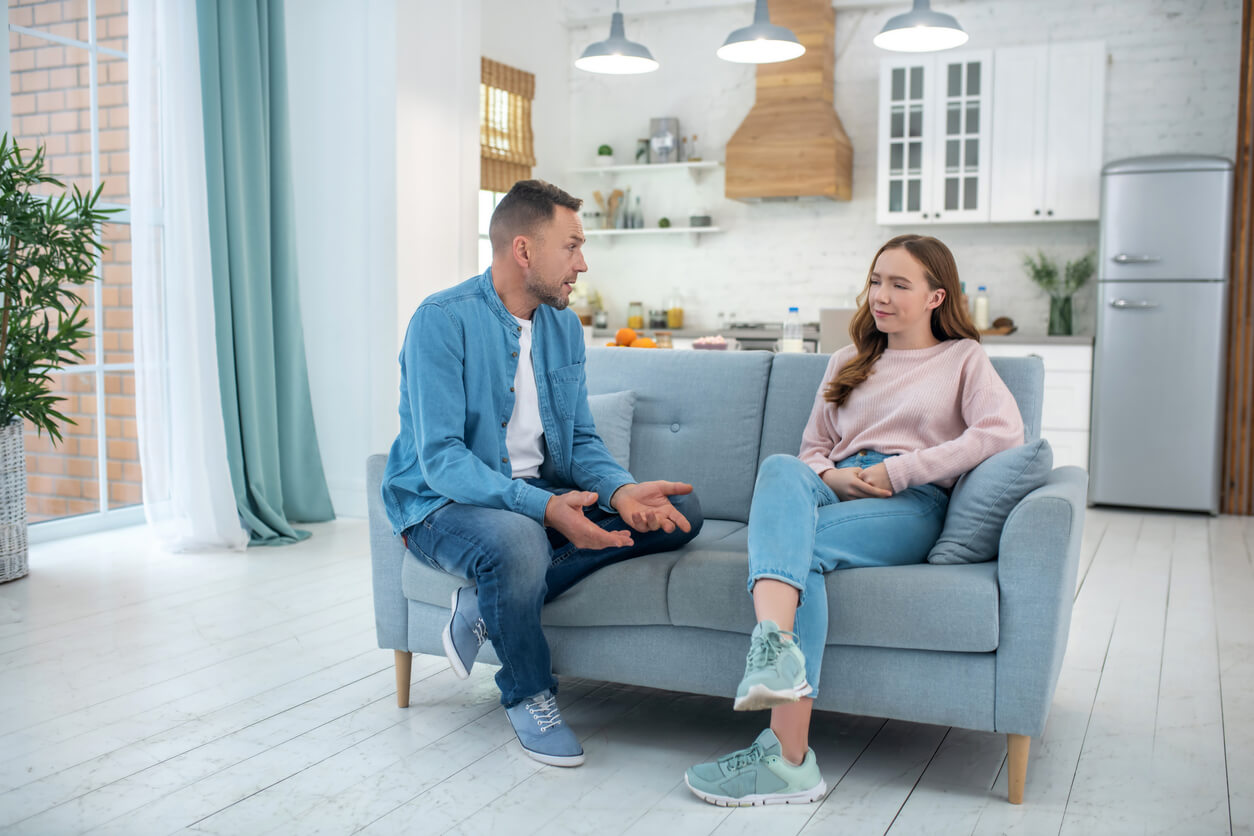 A father and his teenage daughter talking while sitting on the couch.