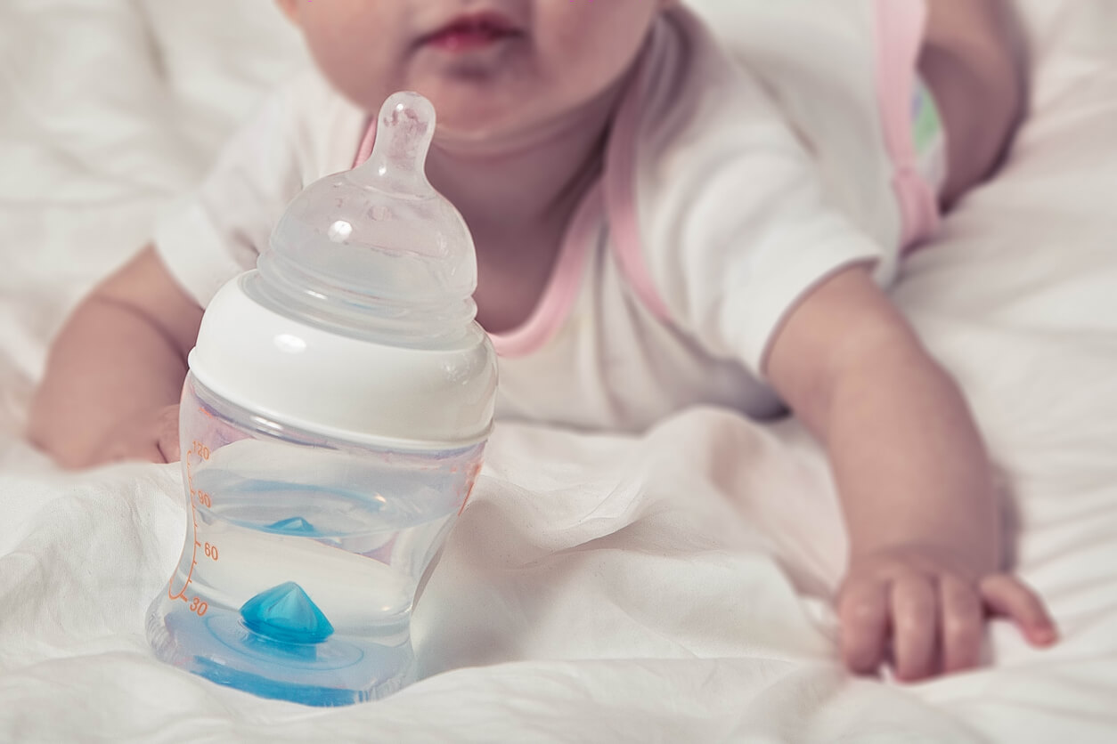 A baby girl lying on her belly near a baby bottle of water.