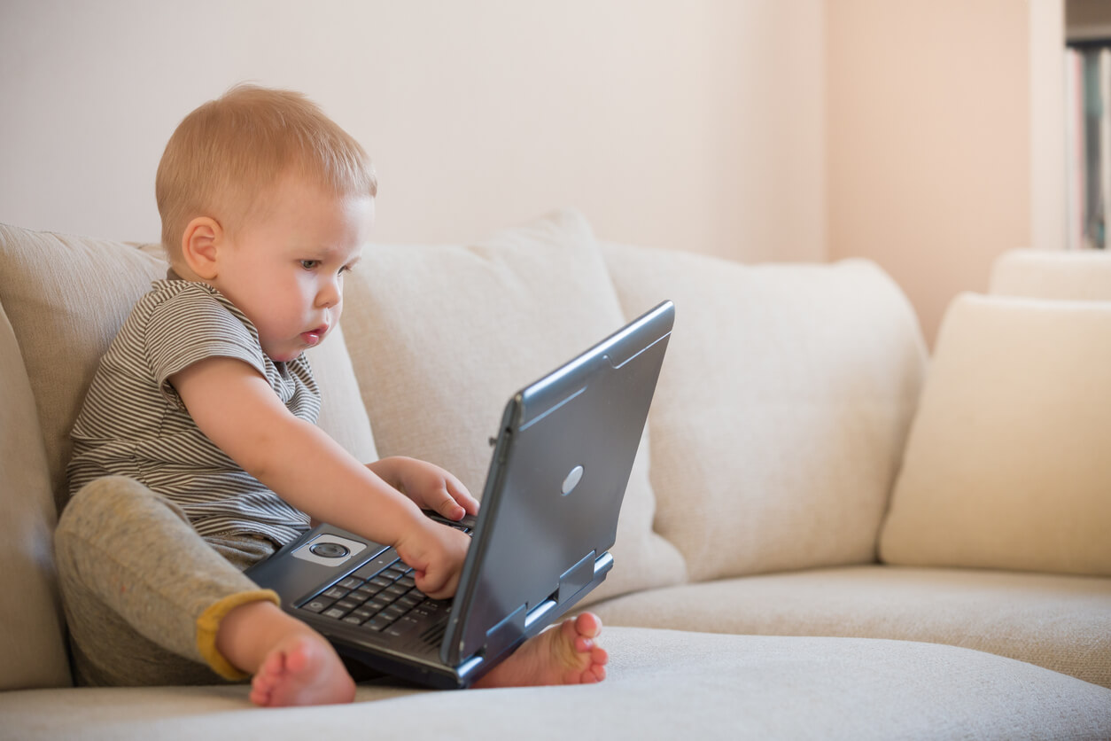 A baby boy playing with a laptop computer.