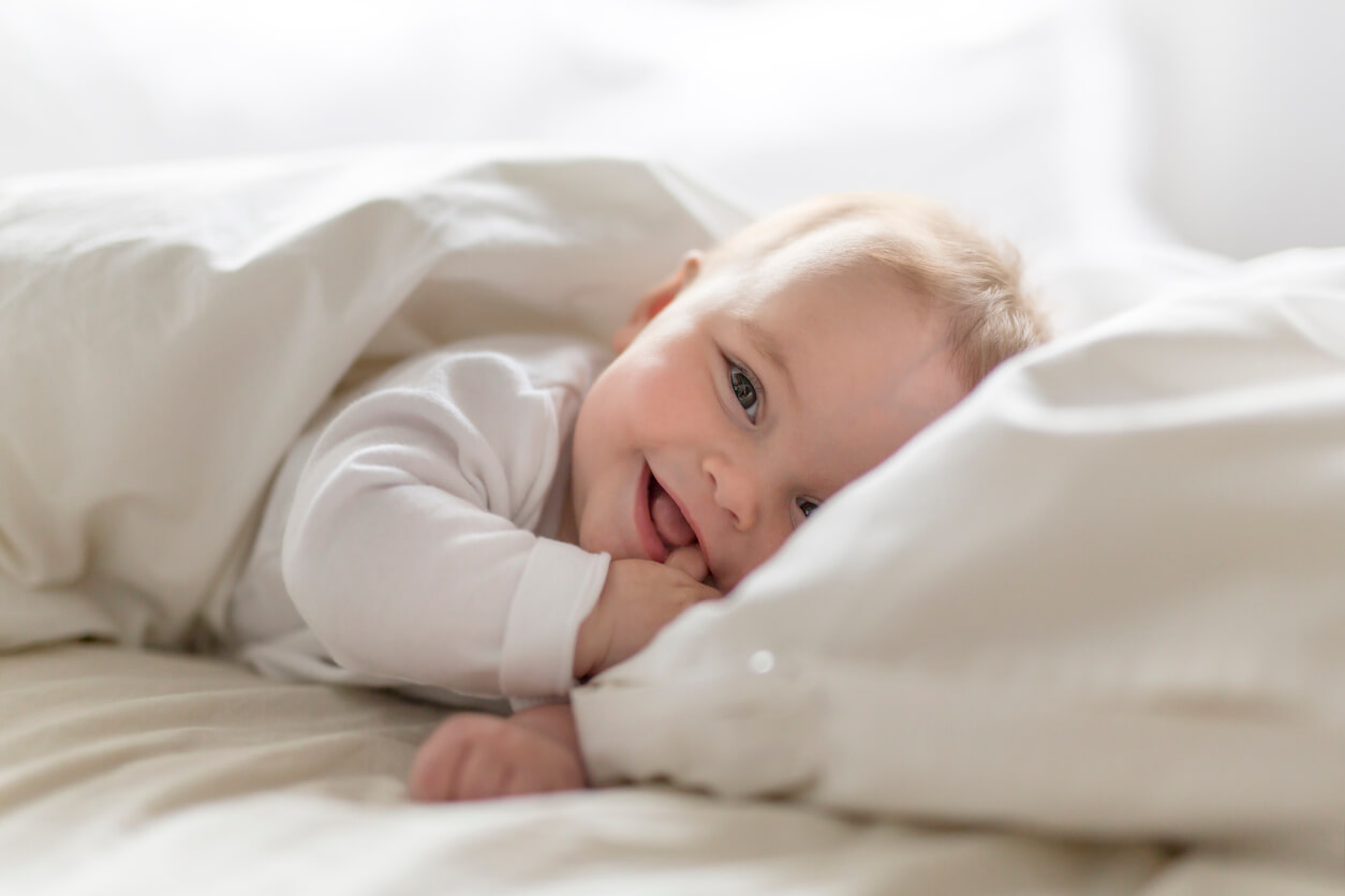 A baby lying in bed smiling.
