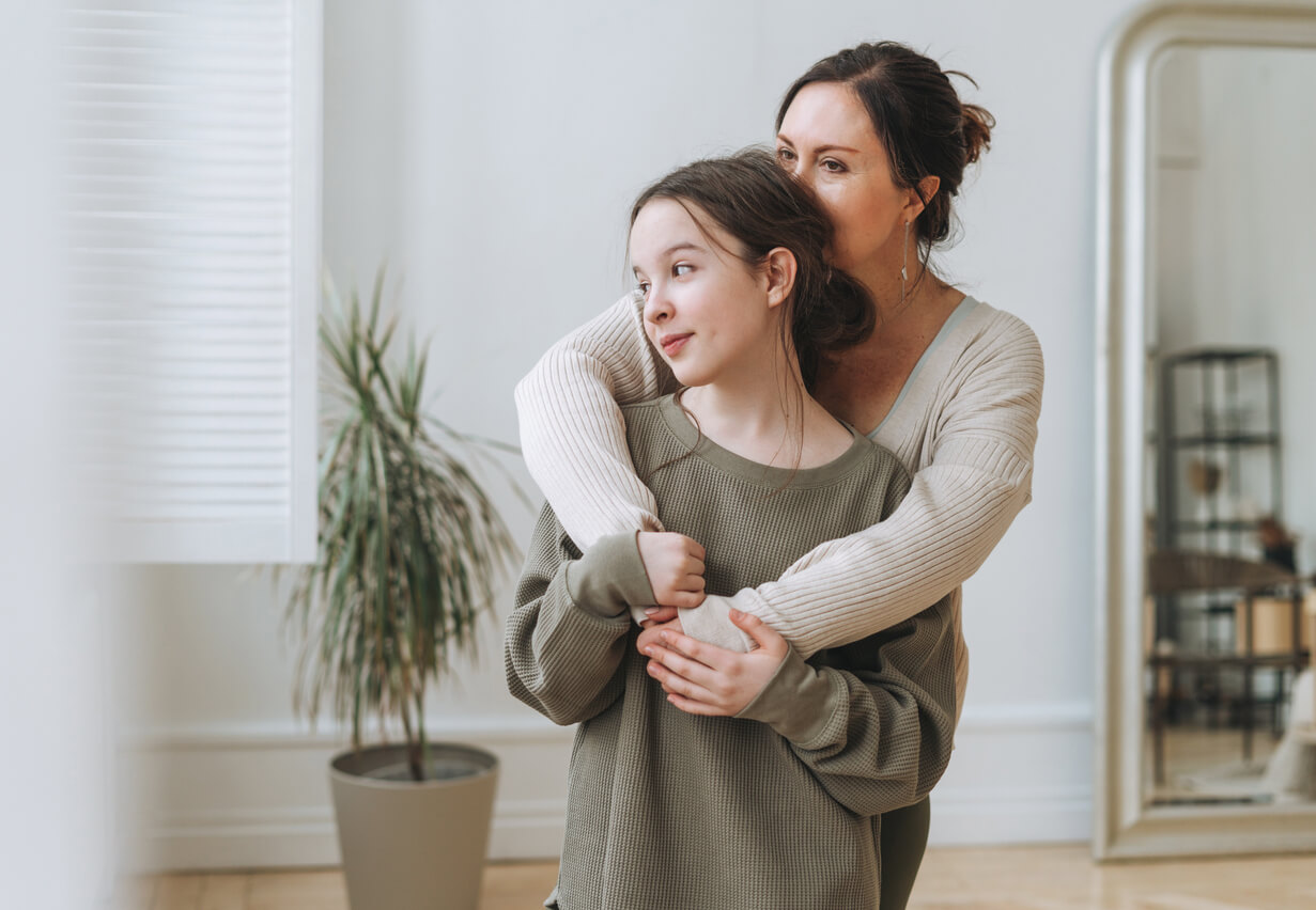 A mother hugging her young teen daughter.