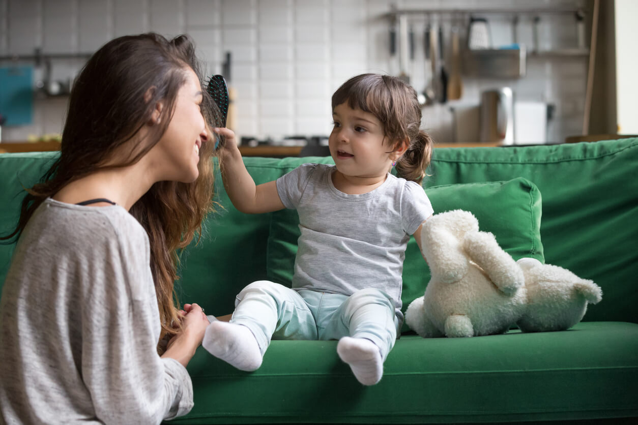 A mother smling while her toddler daughter brushes her hair.