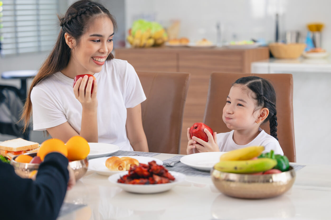 En mor og datter sitter ved bordet og spiser fargerike frukter og grønnsaker.