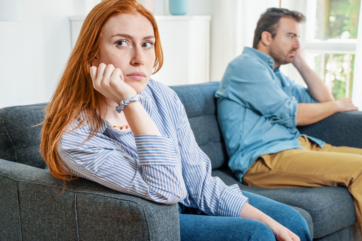 A man and woman sitting on opposite ends of the same couch, looking off in opposite directions.