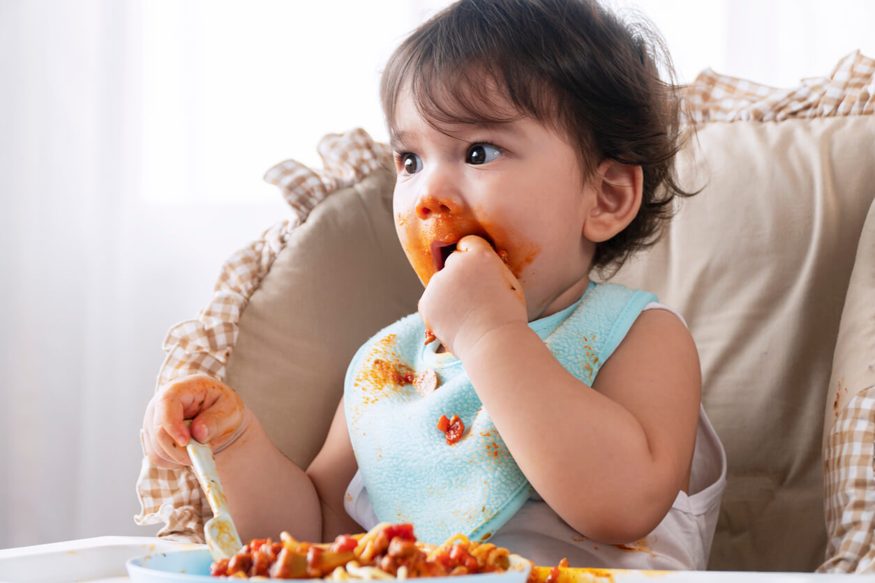 A baby feeding himself from a plate of pasta.