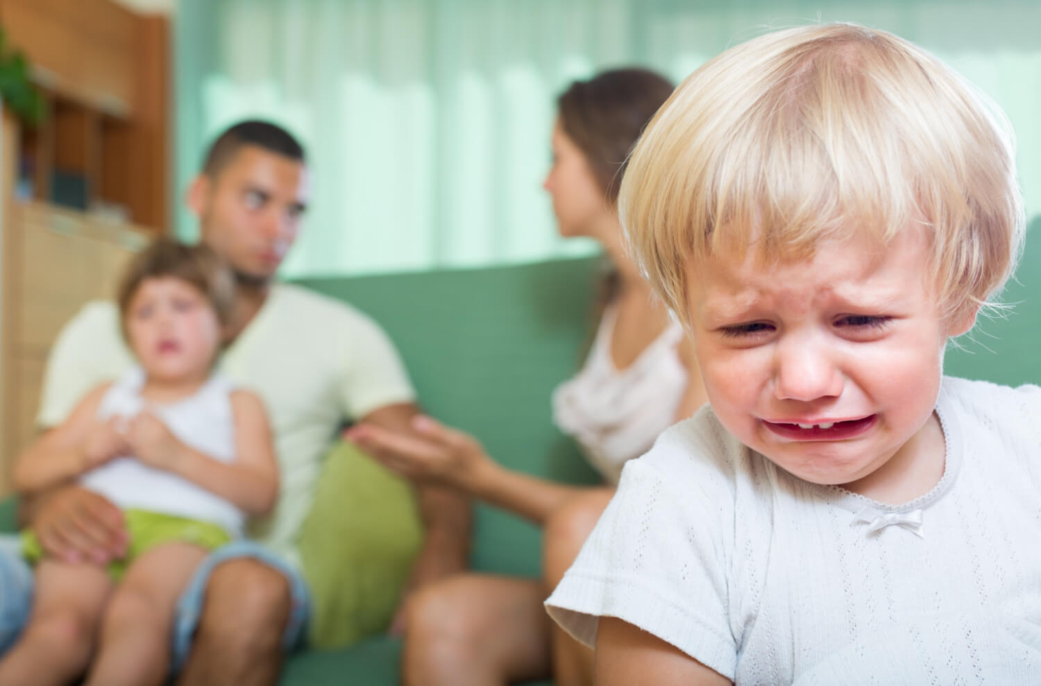En pjokk som gråter mens foreldrene og søskenen hennes sitter i bakgrunnen.