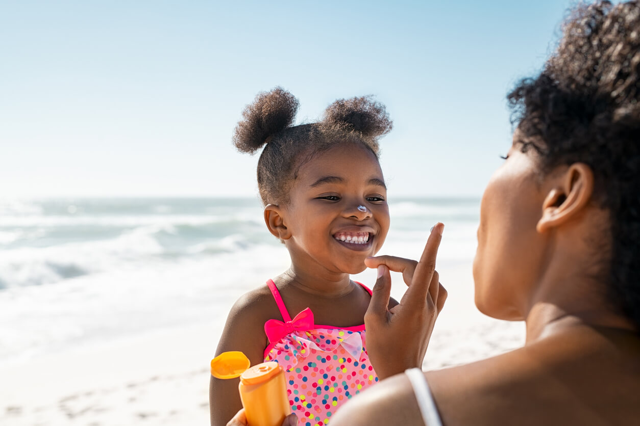 A black mother putting sunscreen on her daughter at the beach.