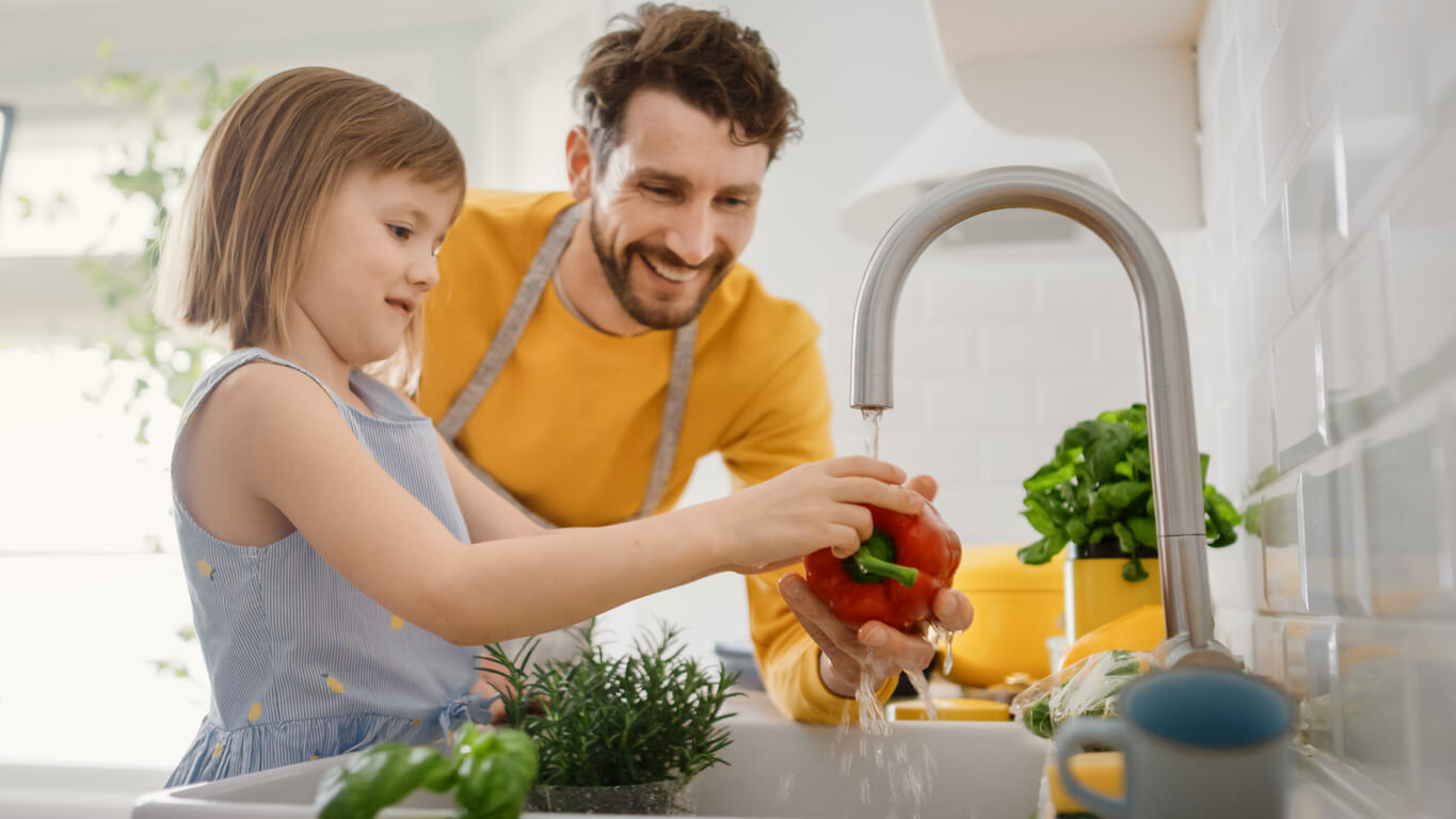 En far og hans unge datter vasker grønnsaker i kjøkkenvasken.