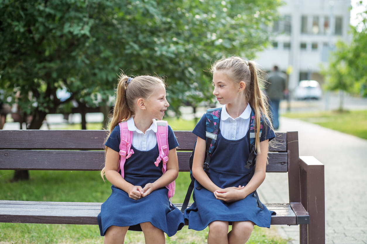 Young school girls sitting on a bench talking.