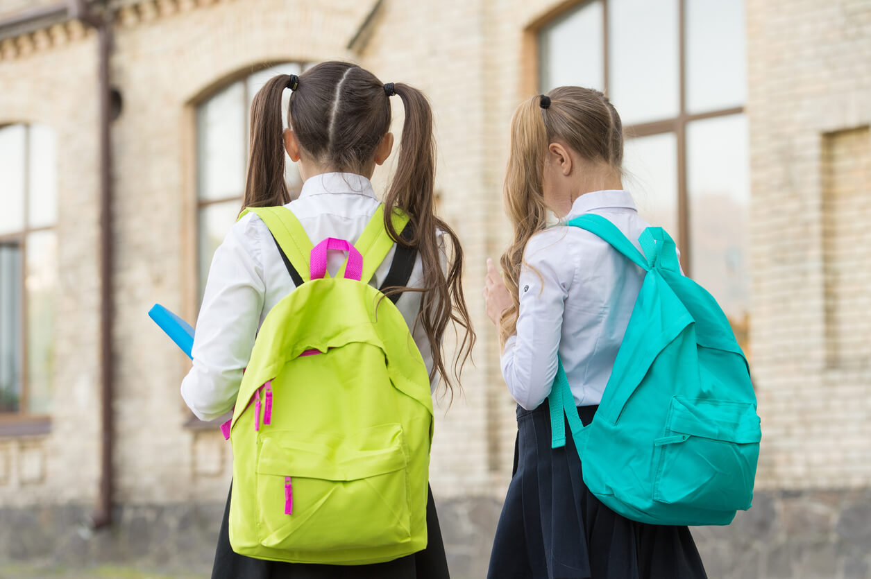 Two school girls wearing backpacks.