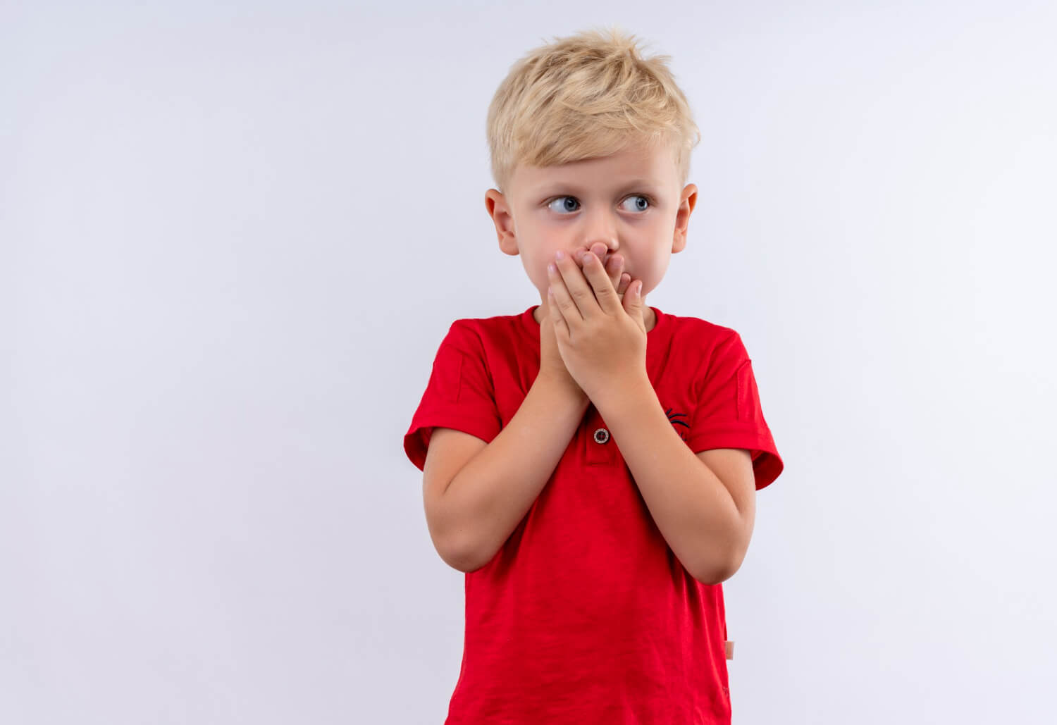 A child looking out of the corner of his eyes and covering his mouth with both hands.