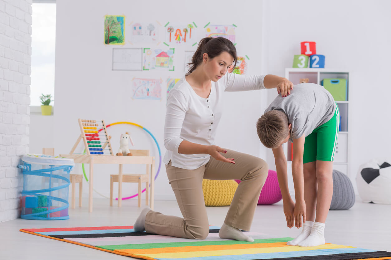 A child stretching downward with the guidance of a physical therapist.