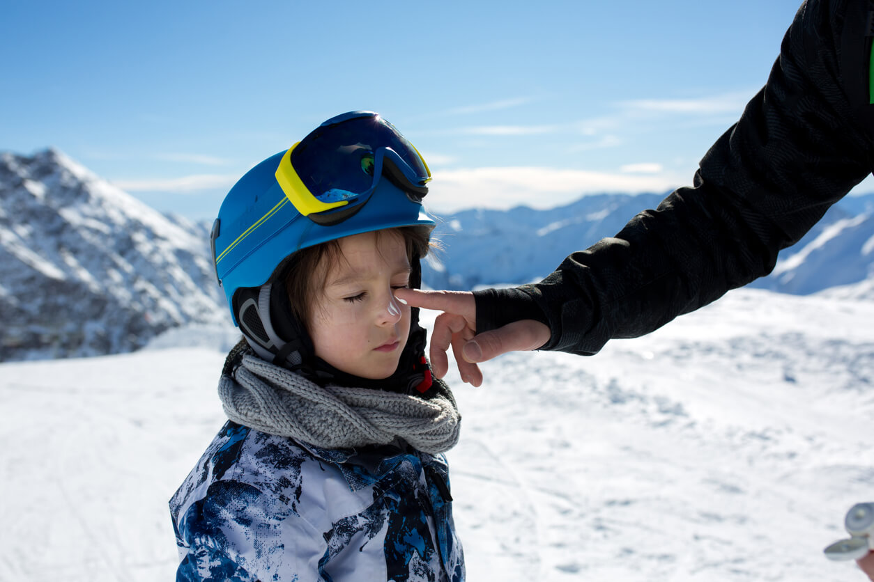 A parent putting sunscreen on a child's face on a ski slope.