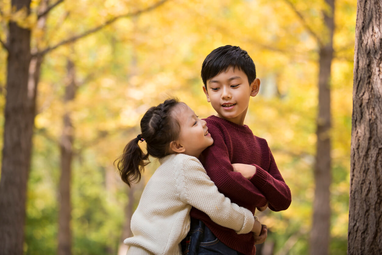 A small Asian girl hugging and older Asian boy in a forest.