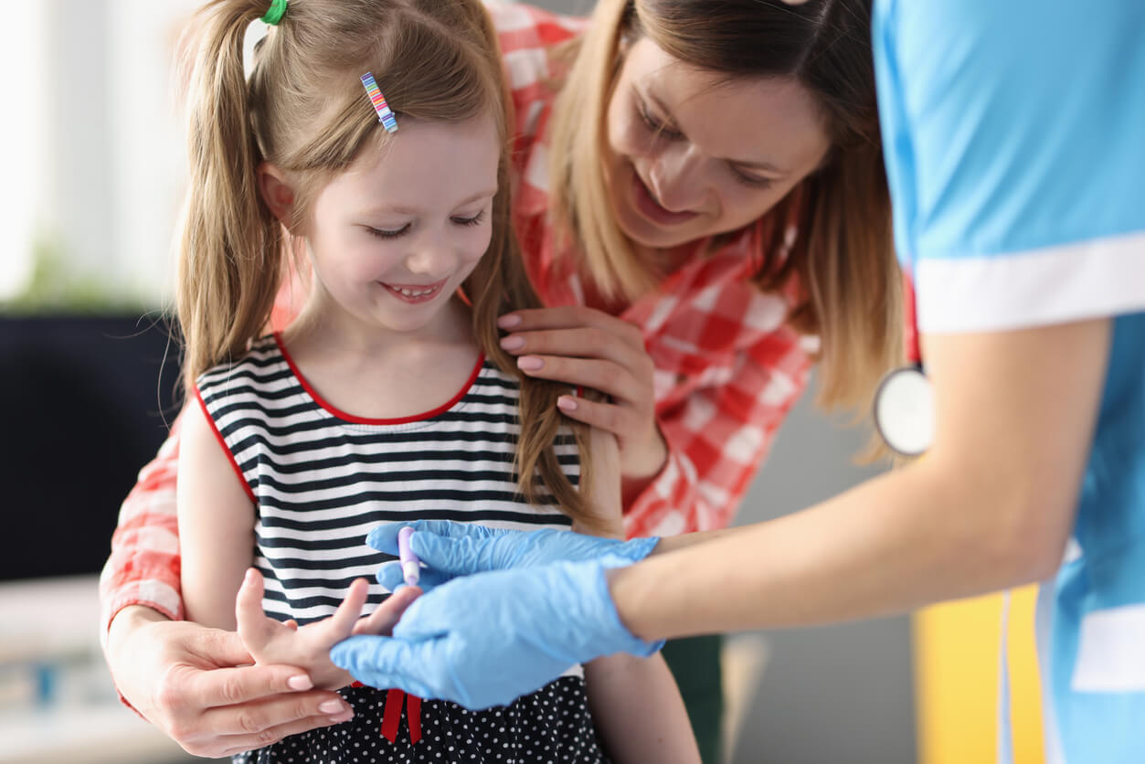A nurse teaching a little girl to test her blood sugar with a pin prick.