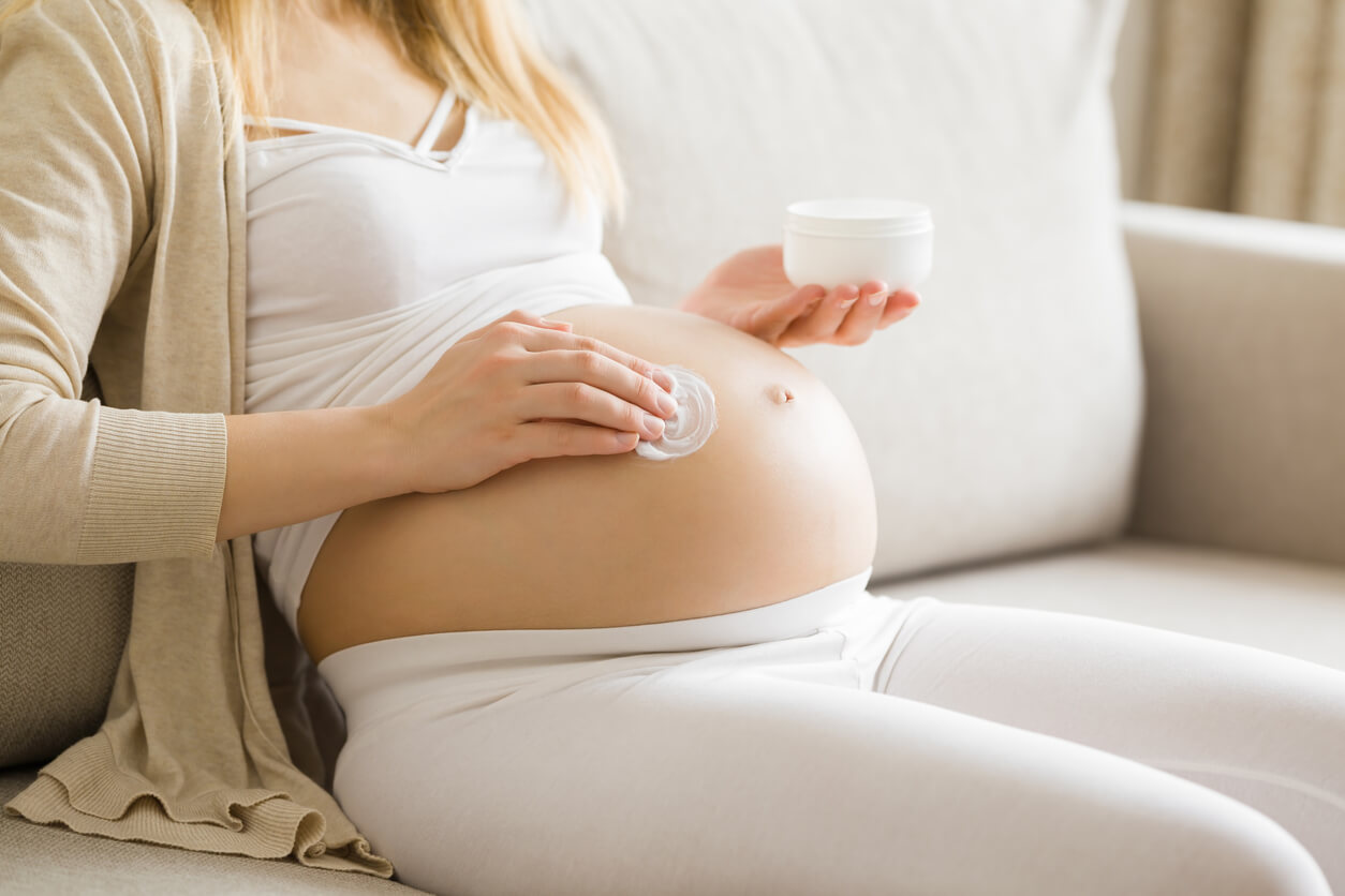 Une femme enceinte qui met de la crème sur son ventre.