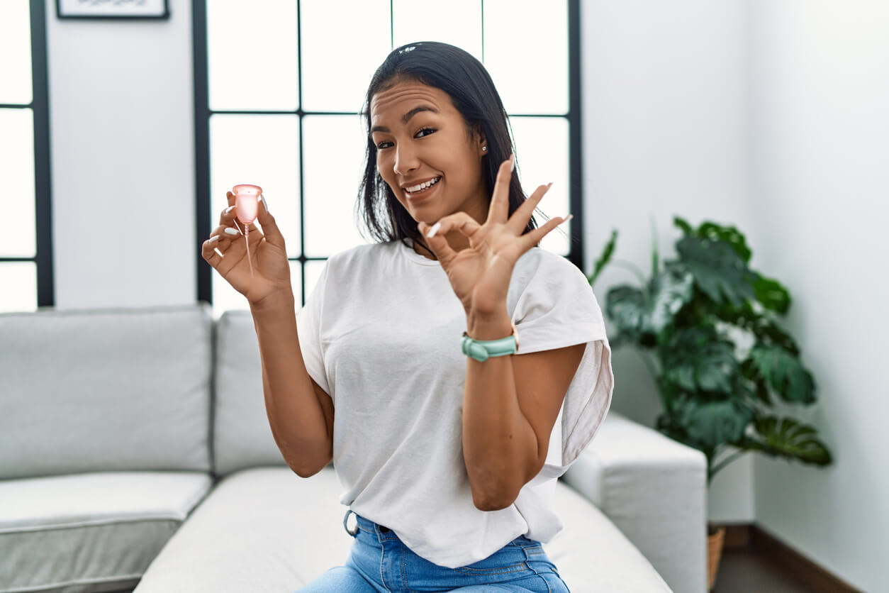 A woman holding a menstrual cup and making the "ok" gesture with her other hand.