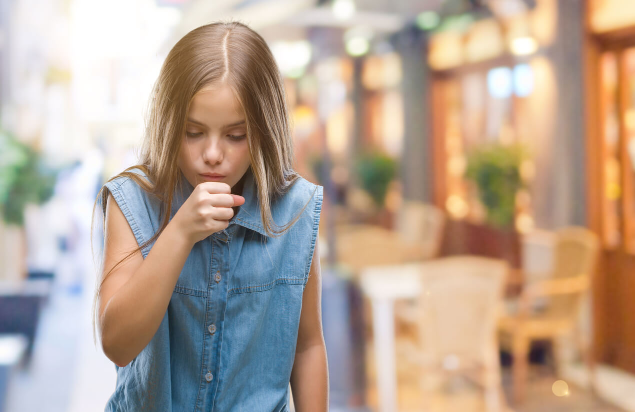 A young girl coughing into her hand.