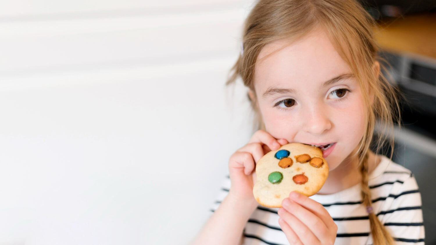 A young girl biting into a cookie.