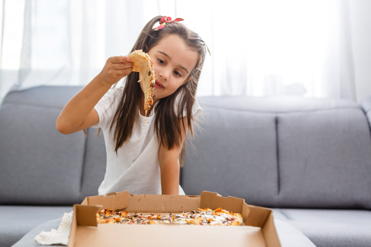 A young girl grabbing a slice of pizza from a delivery box.