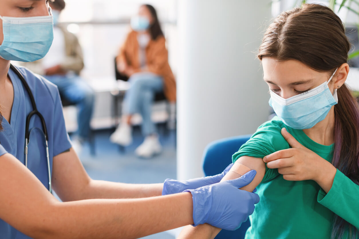 Terveydenhuollon ammattilainen laittaa laastaria tytölle rokotuksen jälkeen.
